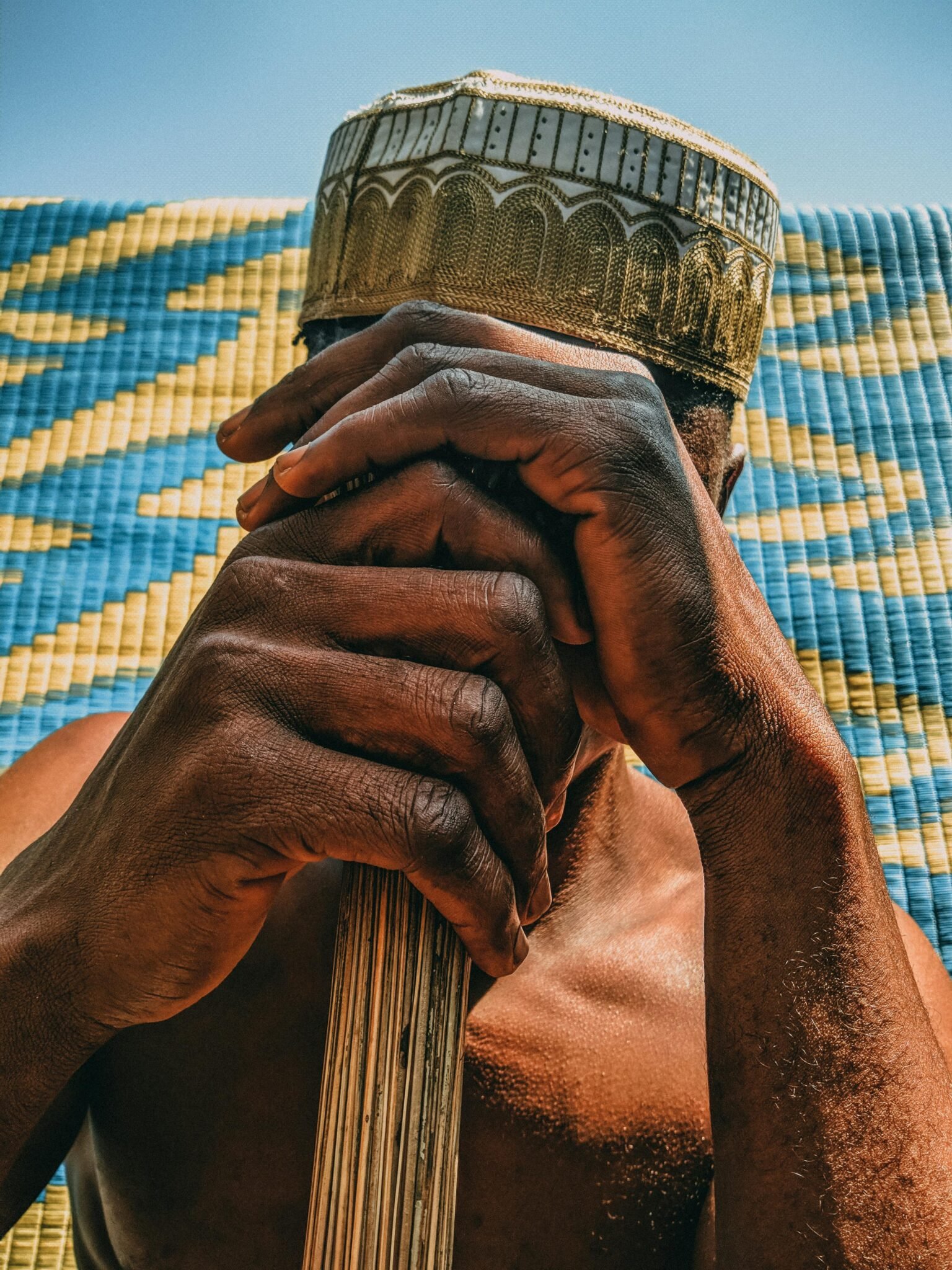 Elderly African man meditating with hands clasped, wearing traditional cap.