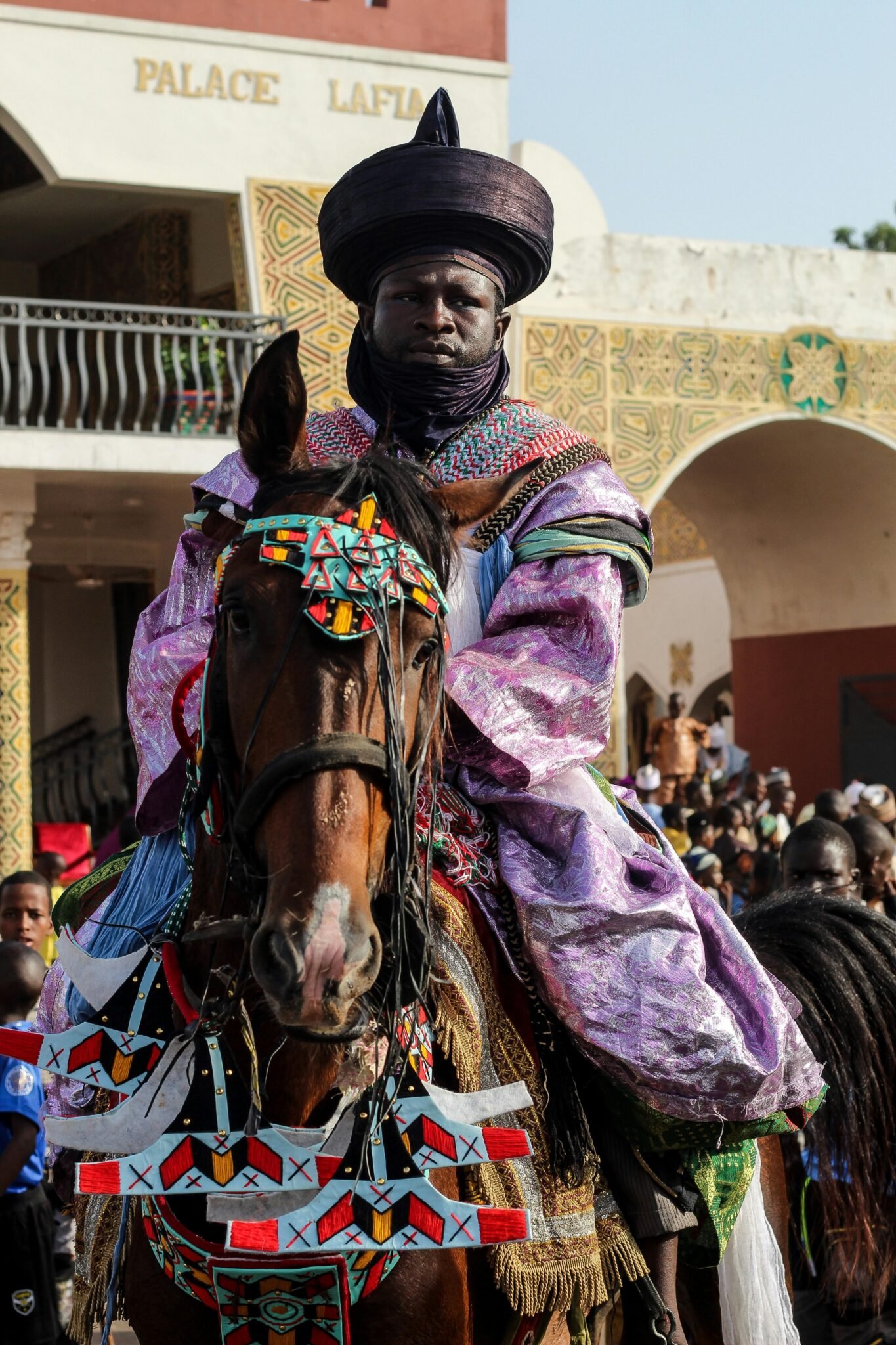 Colorful parade scene featuring a traditionally dressed man riding a decorated horse.